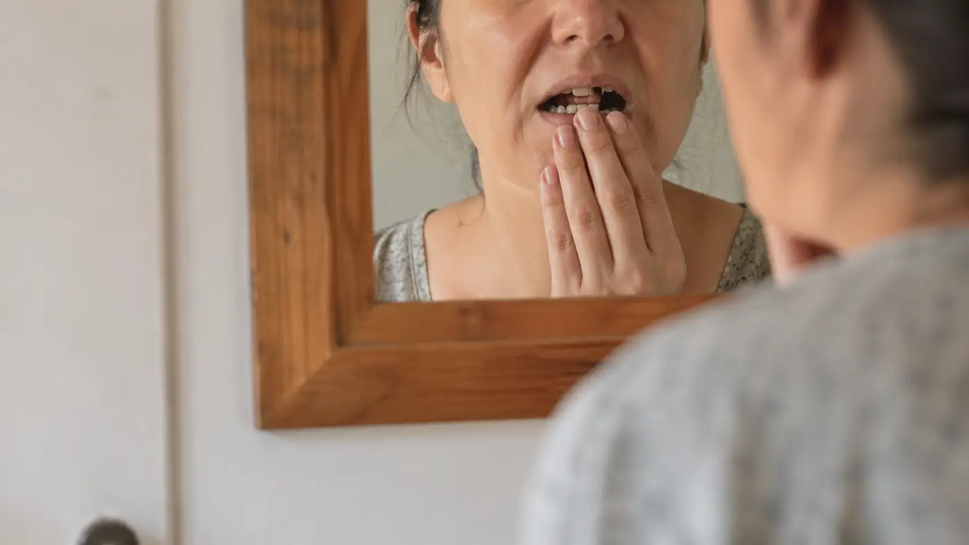 Človek sa pozerá do zrkadla a kontroluje chýbajúci zub, ktorý ovplyvňuje jeho istotu pri úsmeve a rozhovore.